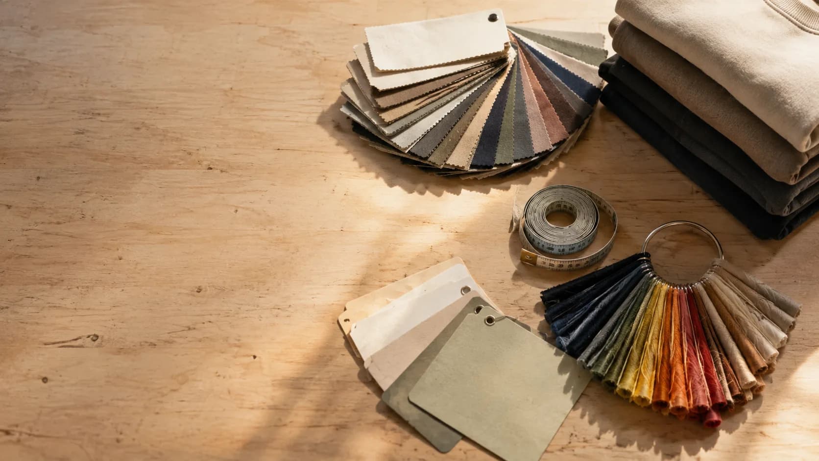 A workbench laid out with fabric swatch cards, a ring of thread colour chips, a tape measure and a stack of folded blanks, seen from above