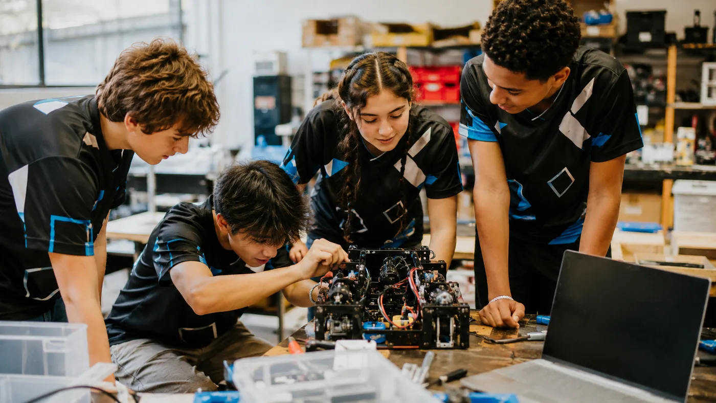 Four Northgate Robotics Club members in matching vinyl-decorated team jerseys working on a competition robot in the school workshop